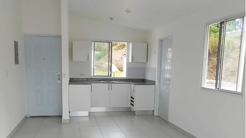 Interior de una casa de Alamedas de Villa Grecia: cocina con gabinetes blancos, sobre de granito y sala-comedor iluminada